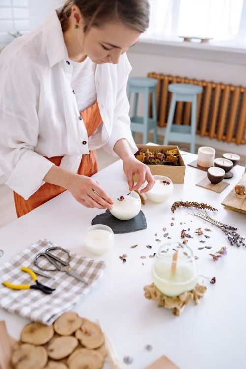 Mujer decorando una vela artesanal con flores secas